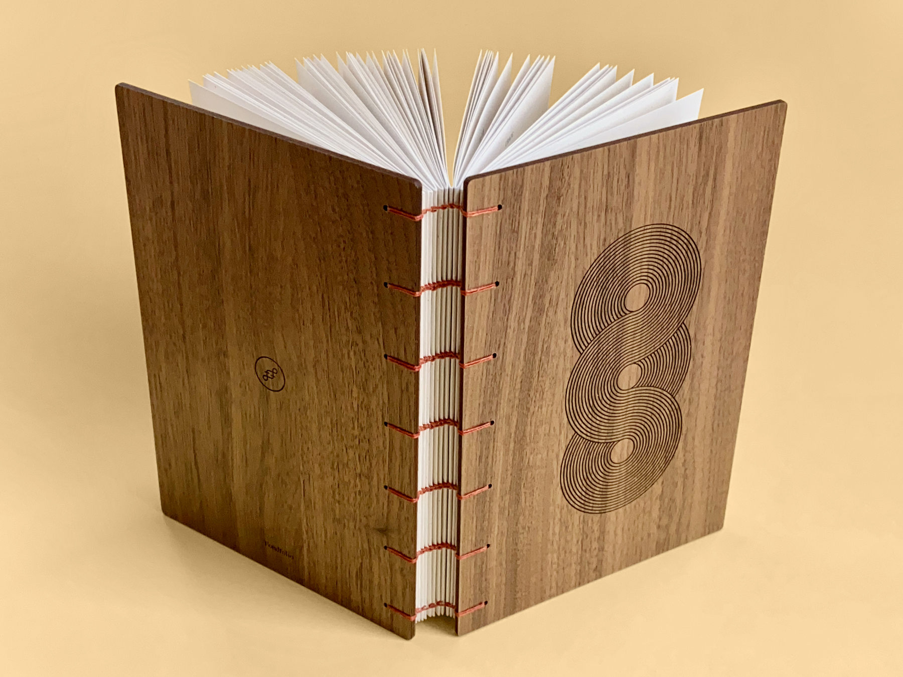 One of our books, opened against a pale yellow background. The covers are made from walnut wood, the book is coptic bound with red stitching.